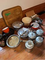 Overview photo showing the full kitchenware lot including all pots, pans, kitchen tools, cutting board, and bowls.