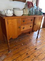 Front view of the vintage pine sideboard showing the two center drawers with metal knobs and side cupboards, with some dishes and glass bottles on top (not included).