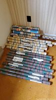 Multiple wallpaper rolls stacked on floor with visible patterns including blue and beige floral, beige with green vertical stripes.