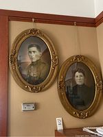 Two oval antique framed portraits hung on a wall, showing a male soldier and a female figure, photographed together to show the lot contents.