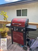 Front angle view of the red-top Brinkmann gas grill with three control knobs, black side shelves, and two wheels.