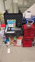 Complete lot stacked with black padded hard case, camera, storage trays, printer ink and more