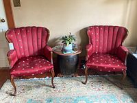 Pair of antique Queen Anne style arm chairs with red patterned upholstery and carved wooden frames, shown side by side with a round side table between them.