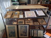 Metal shelf displaying assorted picture frames and prints including two large framed bird nature prints at bottom, several smaller black and white prints, botanical style prints and empty frames.