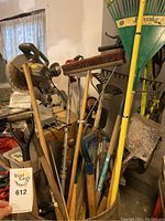 Photo of various garden tools including shovels, broom, rakes, and pitchfork in a container inside a garage or shed.