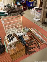 Photo showing the white metal sliding storage rack, brown throw blanket on top, vintage wooden box and assorted hardware pieces including brackets, handles, rods, and packaged curtain accessories.