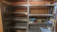 View of two metal shelving units side by side against a wall in a basement or garage, showing overall structure and condition.