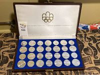 Full view of open wood display case with thirty coins in blue velvet tray, Olympic rings on lid