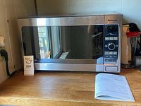Front view of Panasonic microwave oven showing digital control panel, stainless steel finish, and reflective glass door.