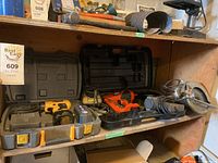 Shelf with various power tools in cases including Dewalt cordless drill and Black & Decker power saw.