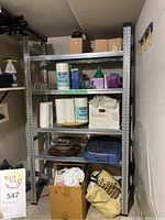 Photo shows a tall metal shelving unit with four adjustable shelves. The shelves hold various household and storage items but the shelving is the lot item.