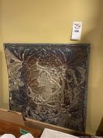 Single pressed tin tile leaning against wall showing embossed central floral medallion and surrounding scrollwork.