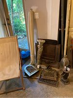 Wide view showing the canvas patio chair, fireplace parts, water pump, and other decor items grouped together against a wall by a door to outside.