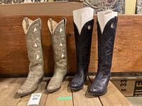 Two pairs of women's cowboy boots standing side by side on a wooden floor with a wooden background, showing front and side views.