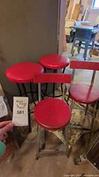 Photo showing two red vinyl bar stools and two red vinyl chairs, all with visible wear and some dents. The stools have round red padded seats with black textured metal legs. Chairs have red backs and seats with metal frames.