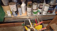 Shelf with multiple used and unopened paint cans of several brands and types including solvents and finishes