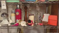 Shelf showing vintage kitchen items including thermos, milkshake maker, pepper grinder, measuring cups and plastic tools.