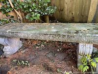 Side view of stone bench showing moss on top and carved supports.