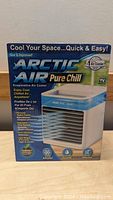 Photo of the Arctic Air Pure Chill evaporative air cooler in its retail packaging, showing branding, features, and images of the product.