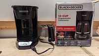 Photo of Black & Decker coffee maker unit with its glass carafe and the original packaging box beside it, showing the product branding and features.