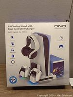 Front image of unopened product box showing the cooling stand, headphone holder, dual controller charger, USB charging ports, and touch switch features.
