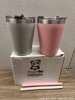 Two Panda Ear 8 oz stainless steel tumblers, one gray and one pink, displayed on a Panda Ear box with two straws in front.