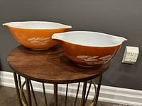 Side angle showing both Pyrex Autumn Harvest Wheat mixing bowls in orange and rust colors, displaying wheat pattern and Cinderella handles.