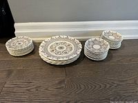 View of six large dinner plates, 11 smaller dessert plates, and 24 tea cup saucers stacked on the floor, showing the full lot quantity and scale.
