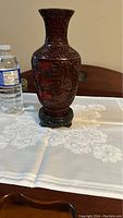 Front view of the cinnabar vase on stand showing detailed carvings and brown lacquer finish.