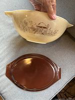 Photo showing cream-colored Pyrex mixing bowl with brown detailed mushroom and foliage pattern, with Cinderella style handles, and solid dark brown oval lid placed beside it.
