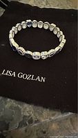 Silver Lisa Gozlan Adore Bracelet laid flat on Lisa Gozlan black pouch highlighting linked charm detail