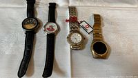 Four vintage wristwatches displayed on white fabric: two Joe Boxer with leather bands, a Kross Swiss with stainless steel bracelet and tag, and a gold-tone Gruen LED watch.