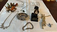 Photo showing assortment of vintage costume jewelry including a Marilyn Monroe themed wristwatch in original box, several rhinestone brooches, bracelets, rings, and necklaces laid out on a white cloth.