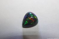 Top view of the pear-shaped black opal cabochon showing vibrant green, red, and blue play-of-color.