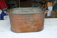 Full view of the used copper tub, showing oval shape, handles, and patina.