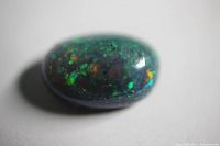 Close-up image of the Ethiopian Black Opal oval cabochon showing vibrant multicolor flashes under light.