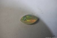 Top view of marquise cabochon fire opal showing orange and green fire colors and translucent body.