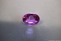 Close-up photo of the oval cut pink sapphire showing its faceted surface and vibrant pink color under strong light.