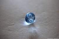 Round faceted blue aquamarine gemstone on flat surface under directional light.