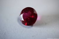 Close-up image of single round cut ruby gemstone showing facets and deep red color, highlighting clarity and cut shape.