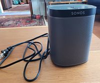 Photo of Sonos Play:1 wireless speaker on a wooden surface, showing the speaker and power cord.