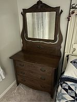 Front angle view of antique dresser showing three wooden drawers, metal handles, and the attached mirror with carved frame. Visible wood grain and carved ornamentation.