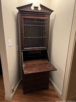 Antique solid wood secretary desk with drop-front writing surface open and glass door on upper cabinet closed