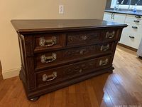 Front view of antique wooden sideboard showing ornate carved drawer fronts and metal drawer handles.