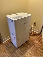 Front and side view of the white Noma dehumidifier showing the air vents, control panel on top, and power cord plugged into the wall.