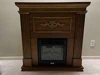 Front view of the electric fireplace with wooden mantel frame showing decorative carvings and the electric insert with glass front.