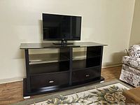 Front view of the entertainment unit with a mounted TV showing its glass top and dual shelving with drawers below.