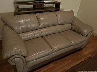 Front side view of taupe faux leather couch with three seat cushions and rolled arms, showing condition and overall shape.