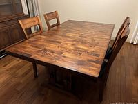 Rectangular wood dining table with four chairs around it, showing wood grain and finish