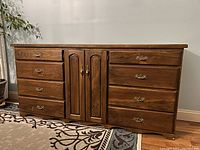 Front view of the large wooden dresser showing 6 drawers (3 on each side) and 2 cabinet doors in the center with brass handles.